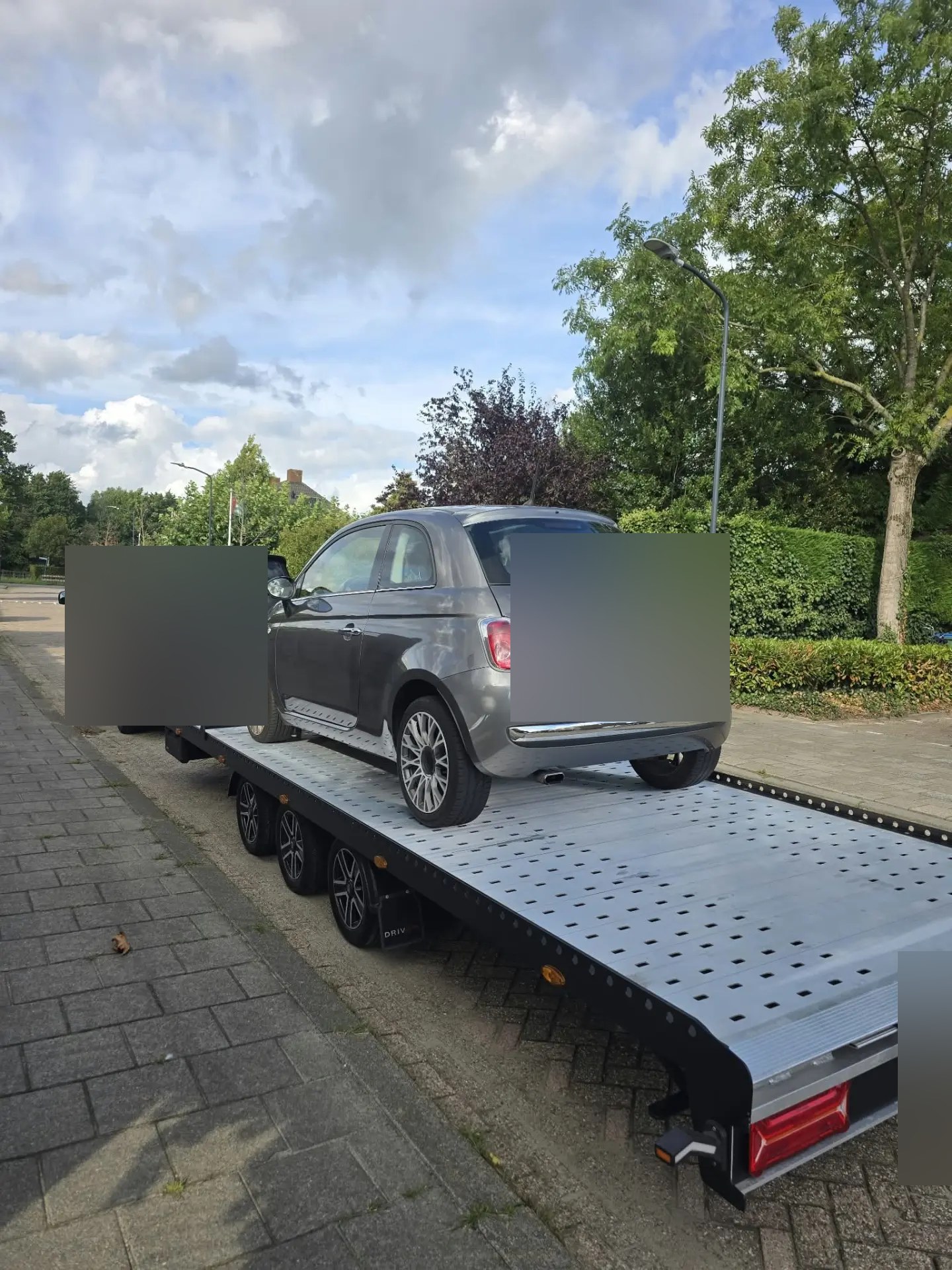 Kleine personenauto op een autotrailer achter een bestelbus